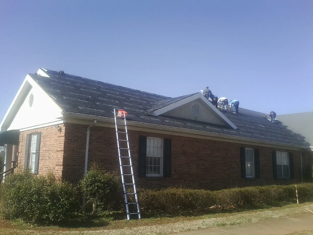 Crew tearing shingles off a brick ranch roof with a ladder set — Emergency Roof Repair work by our crew in Pawleys Island