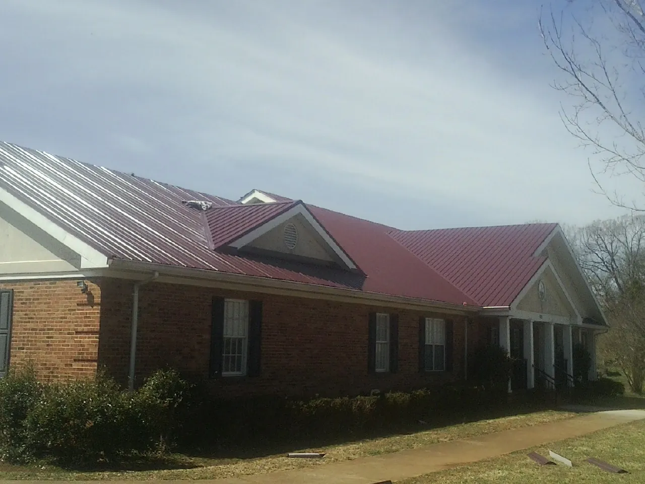 Red metal roof with gabled entries on a long brick building, from a Hail Damage Roof Repair job in Pawleys Island