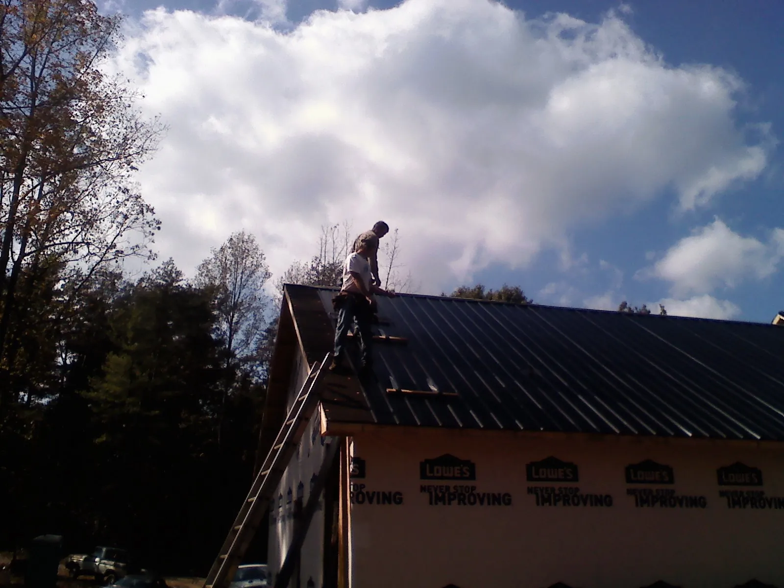 Roofer fastening dark metal panels high against a cloudy sky, from a Roof Inspection job in Pawleys Island
