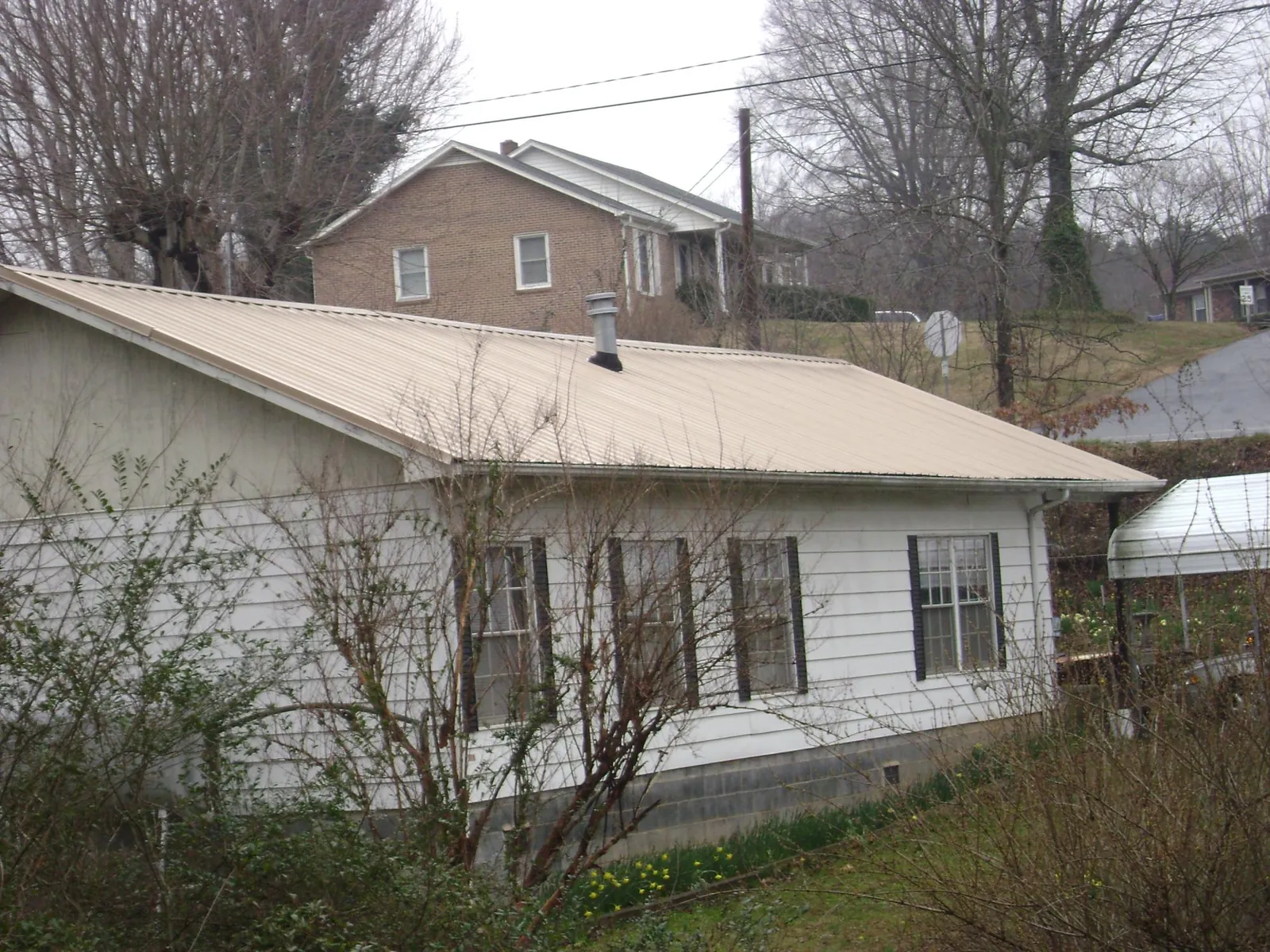 Tan metal roof on a white sided house set into a hillside — Commercial Roofing by Roofing Brothers in Pawleys Island